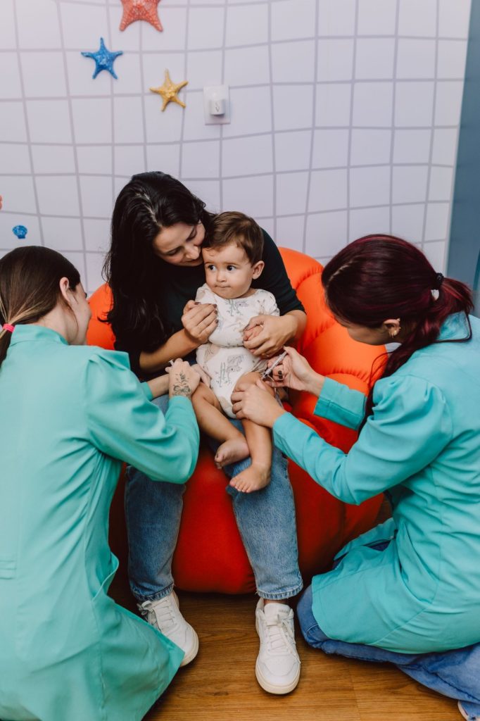 Bebê no colo da mãe recebendo vacinas da equipe Imunoclinic no espaço infantil