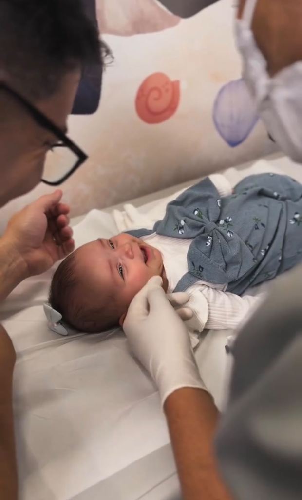 Profissional da Imunoclinic segurando com cuidado a cabeça de um bebê deitado na maca